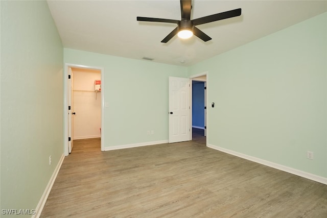 unfurnished bedroom featuring a walk in closet, a closet, light hardwood / wood-style flooring, and ceiling fan