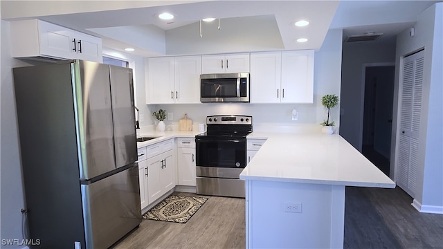 kitchen featuring kitchen peninsula, white cabinetry, stainless steel appliances, and wood-type flooring