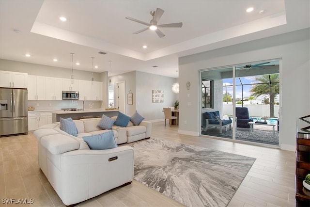 living room featuring a raised ceiling, ceiling fan, and light wood-type flooring