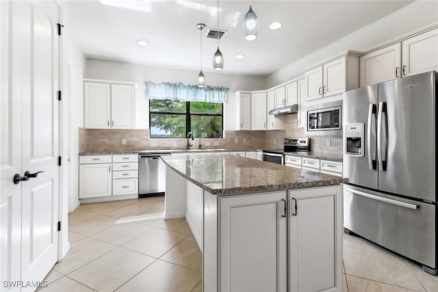 kitchen with white cabinets, hanging light fixtures, appliances with stainless steel finishes, dark stone counters, and a center island