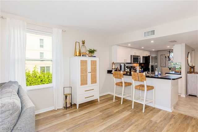 kitchen featuring a kitchen breakfast bar, light hardwood / wood-style floors, kitchen peninsula, stainless steel appliances, and white cabinets