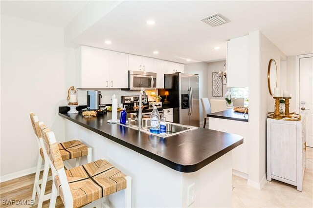 kitchen with a kitchen breakfast bar, stainless steel appliances, sink, kitchen peninsula, and white cabinetry