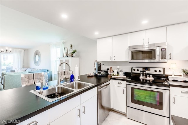 kitchen with stainless steel appliances, dark countertops, a sink, and white cabinetry