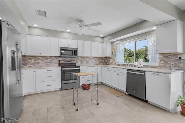 kitchen featuring stainless steel appliances, white cabinetry, sink, ceiling fan, and decorative backsplash