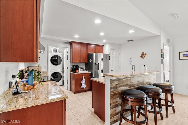 kitchen with light stone countertops, a kitchen island, vaulted ceiling, stainless steel fridge with ice dispenser, and stacked washer and clothes dryer