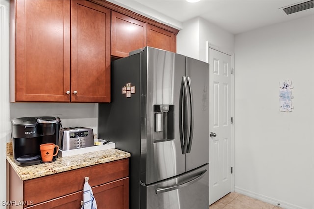 kitchen featuring light tile patterned flooring, stainless steel fridge, and light stone counters