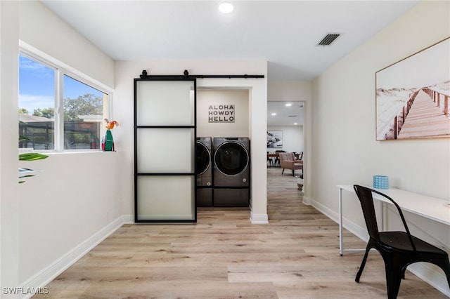 laundry area with light wood finished floors, a barn door, independent washer and dryer, and baseboards