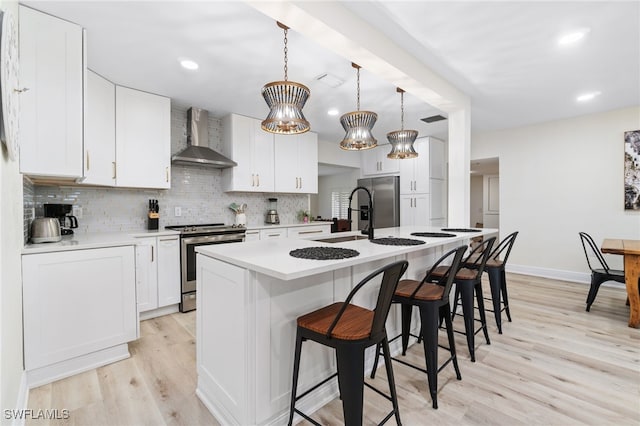 kitchen featuring a breakfast bar, light wood finished floors, stainless steel appliances, tasteful backsplash, and wall chimney exhaust hood