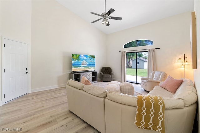 living area with high vaulted ceiling, a ceiling fan, light wood-style flooring, and baseboards