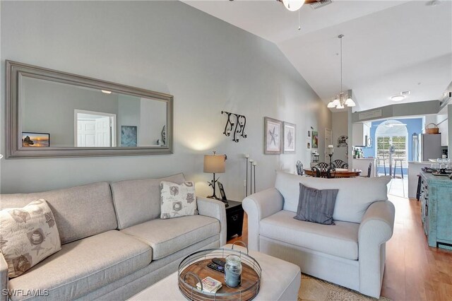 living room featuring lofted ceiling, ceiling fan with notable chandelier, and light hardwood / wood-style floors