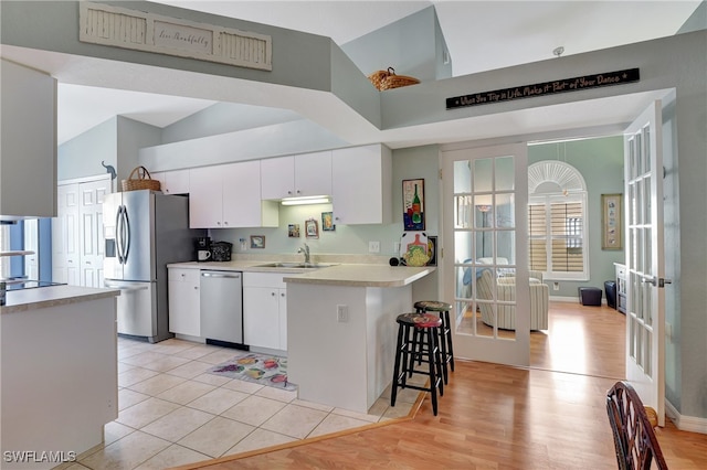 kitchen with stainless steel appliances, sink, white cabinetry, and light hardwood / wood-style floors