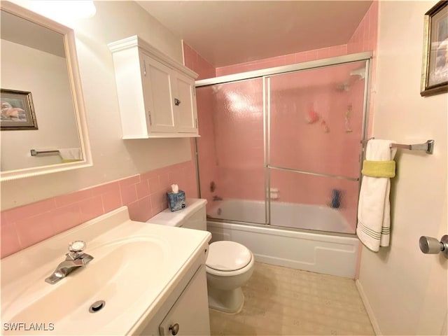 bathroom featuring toilet, bath / shower combo with glass door, tile walls, and vanity