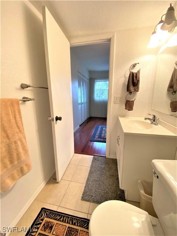 bathroom featuring a textured ceiling, tile patterned flooring, toilet, vanity, and baseboards