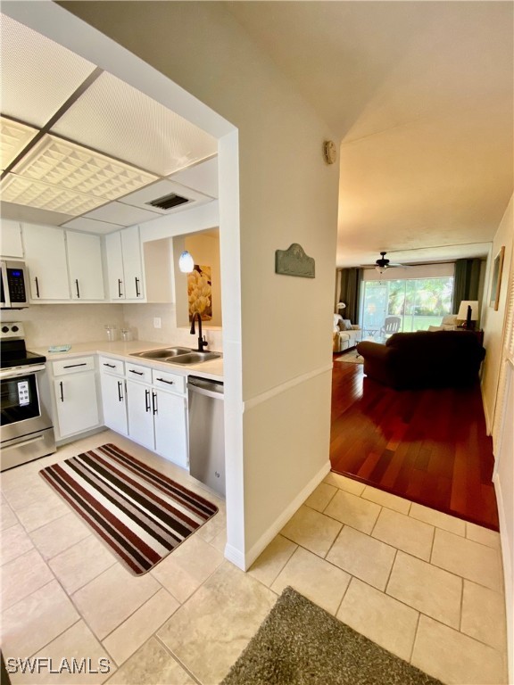 kitchen with appliances with stainless steel finishes, white cabinetry, light tile patterned floors, and sink