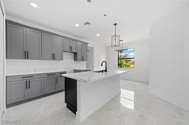 kitchen with an island with sink, light stone counters, sink, and gray cabinetry