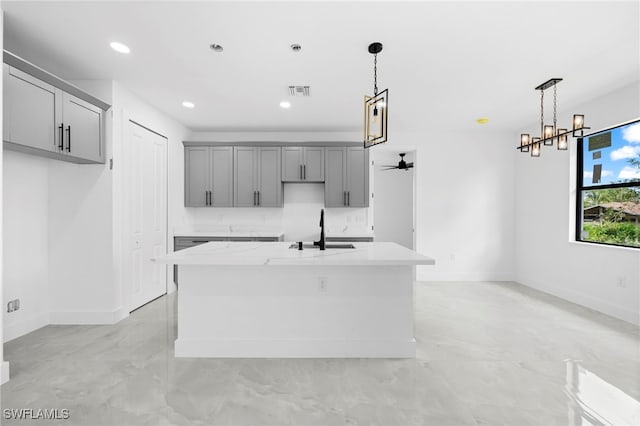 kitchen with a kitchen island with sink, gray cabinets, decorative light fixtures, light stone counters, and sink