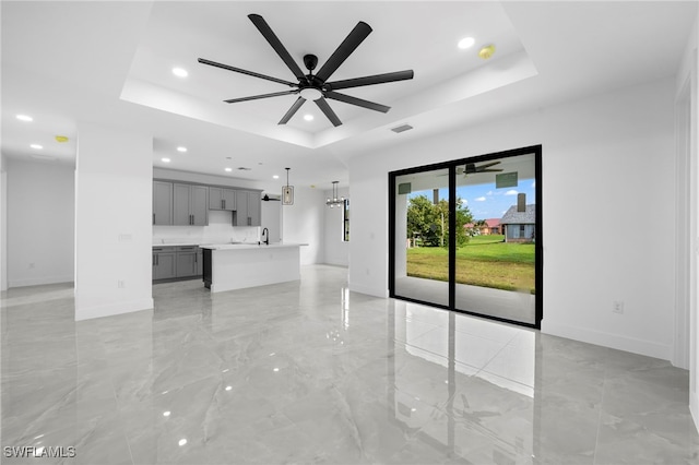 unfurnished living room featuring a raised ceiling, ceiling fan, and sink