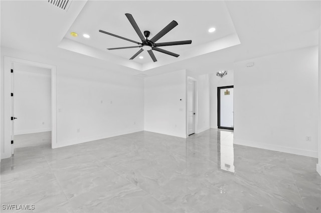 empty room with ceiling fan and a raised ceiling