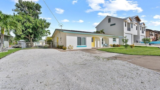 view of front of house with a front yard, gravel driveway, fence, and stucco siding