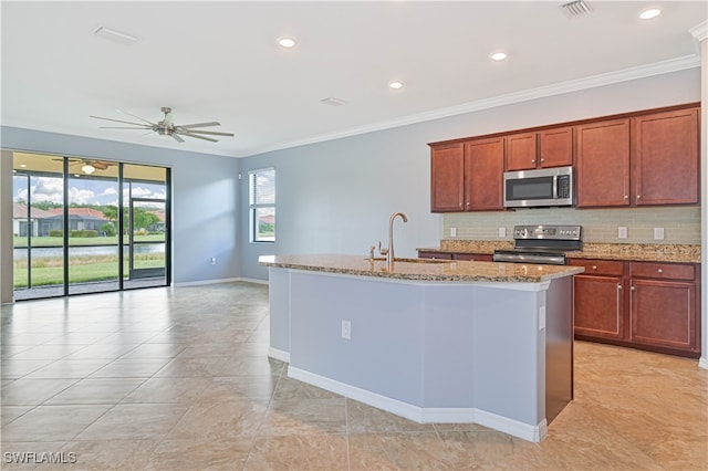 kitchen with light stone countertops, stainless steel appliances, sink, an island with sink, and ceiling fan