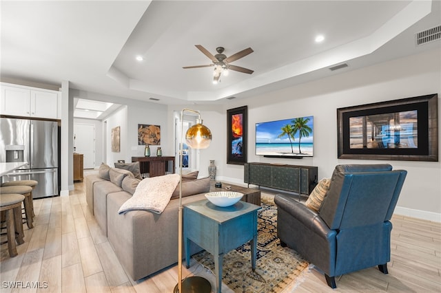 living room with ceiling fan, light hardwood / wood-style floors, and a tray ceiling