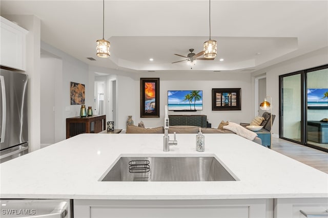 kitchen with light stone counters, a sink, open floor plan, a raised ceiling, and white cabinets