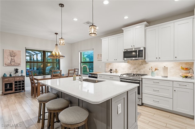 kitchen featuring white cabinets, a center island with sink, sink, hanging light fixtures, and stainless steel appliances