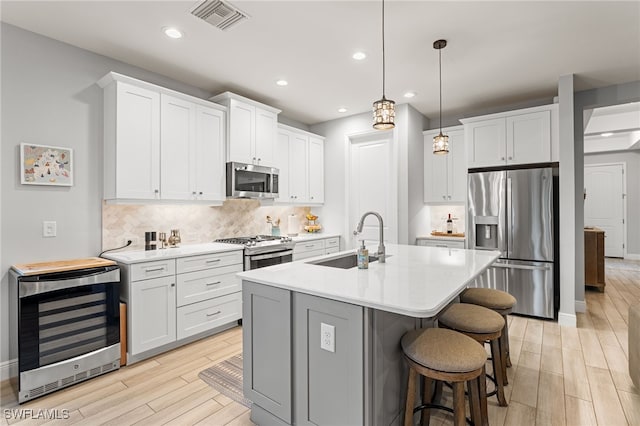 kitchen featuring white cabinets, sink, decorative light fixtures, stainless steel appliances, and beverage cooler