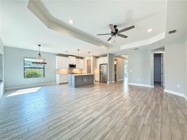 13840 Amblewind Cove Way, Fort Myers, FL 33905 - unfurnished living room with a raised ceiling, light wood-style floors, ceiling fan, a sink, and baseboards