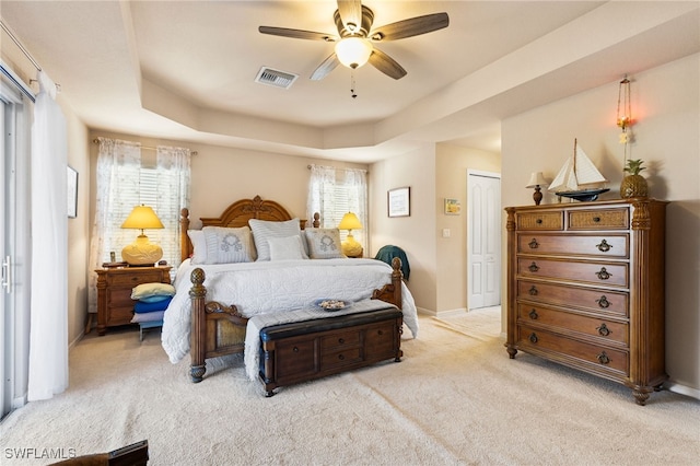 carpeted bedroom featuring a closet, a raised ceiling, multiple windows, and ceiling fan