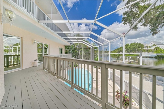 wooden terrace featuring glass enclosure, a water view, and an outdoor pool