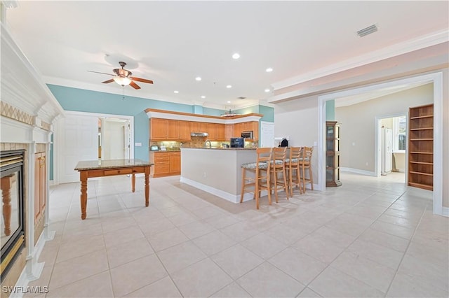 kitchen featuring light tile patterned flooring, a peninsula, a fireplace, ornamental molding, and stainless steel microwave