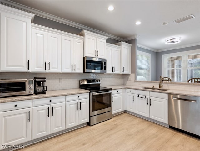 kitchen with white cabinets, light wood-type flooring, stainless steel appliances, sink, and ornamental molding