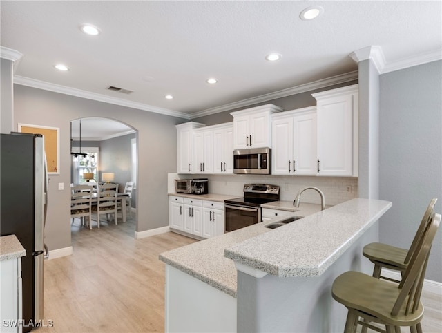 kitchen with light hardwood / wood-style flooring, stainless steel appliances, white cabinets, and a breakfast bar