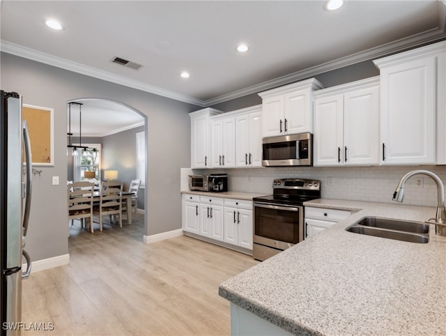 kitchen with light wood-type flooring, ornamental molding, stainless steel appliances, sink, and white cabinets