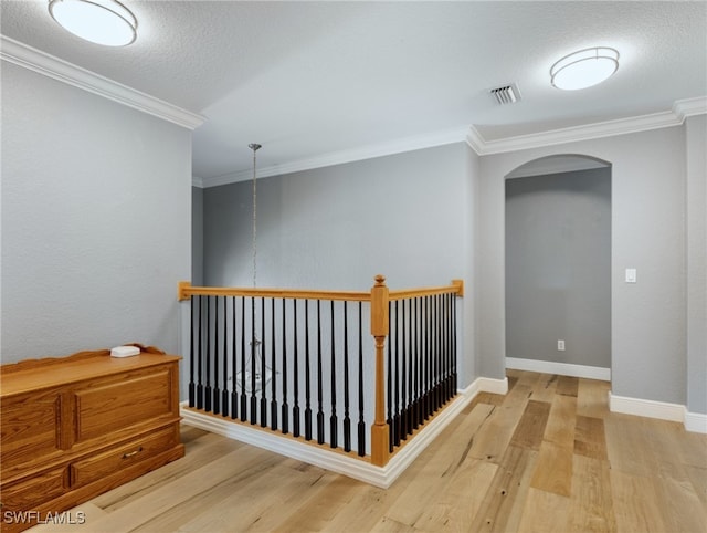 hallway featuring light wood-type flooring, crown molding, and a textured ceiling