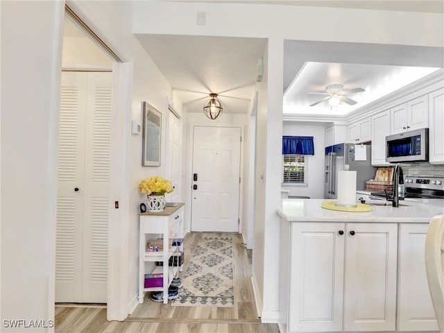 kitchen with decorative backsplash, ceiling fan, appliances with stainless steel finishes, white cabinets, and light hardwood / wood-style floors