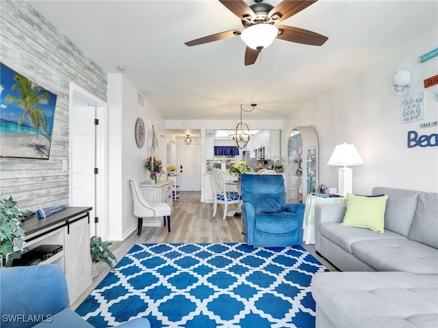 living room featuring ceiling fan with notable chandelier and light hardwood / wood-style flooring