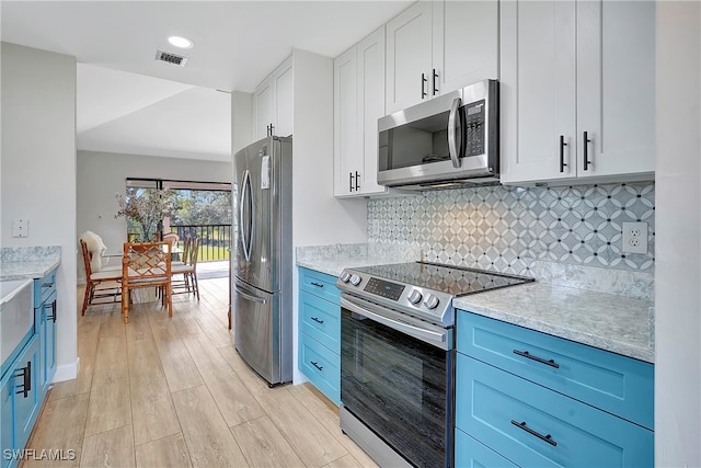 kitchen with light wood-type flooring, appliances with stainless steel finishes, decorative backsplash, and blue cabinetry