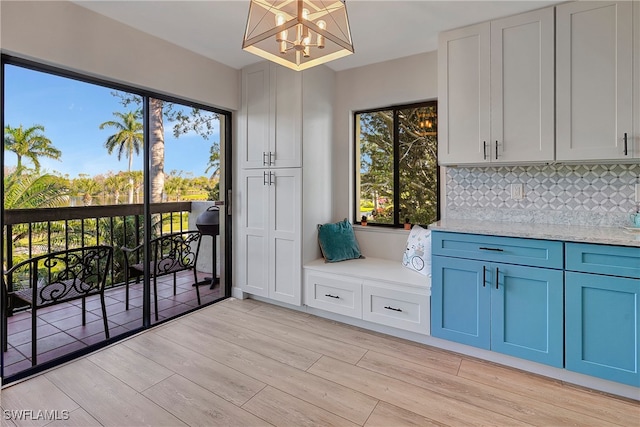 interior space featuring light stone countertops, a notable chandelier, blue cabinetry, tasteful backsplash, and light wood-type flooring