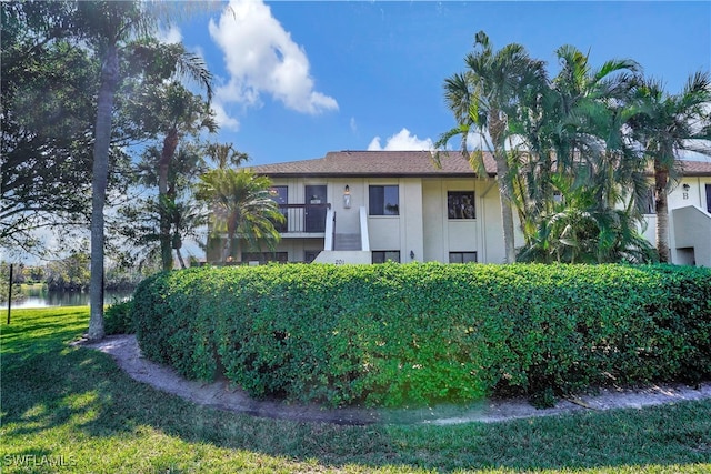 view of front of home with a balcony, a water view, and a front lawn