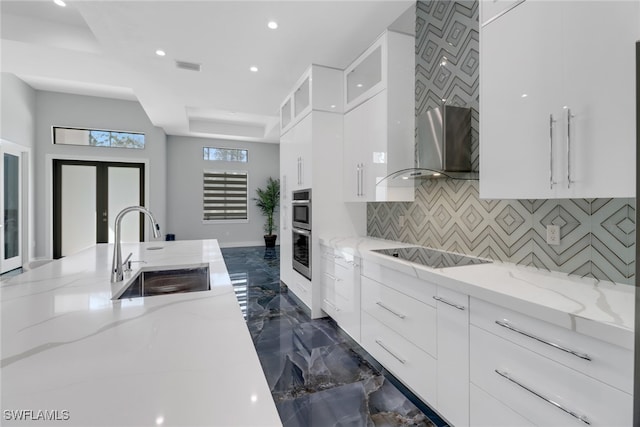 kitchen with black electric stovetop, light stone countertops, sink, backsplash, and white cabinets