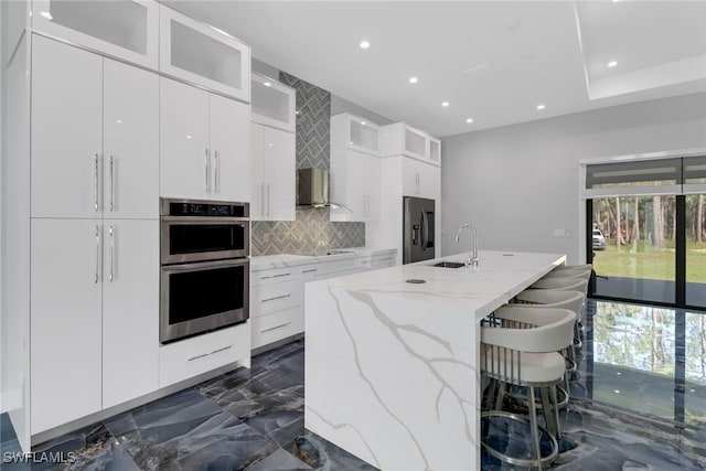 kitchen with sink, white cabinetry, stainless steel appliances, and an island with sink