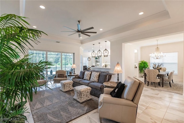 living room with a tray ceiling and ceiling fan with notable chandelier