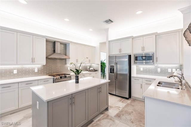 kitchen featuring decorative backsplash, a center island, stainless steel appliances, and wall chimney range hood