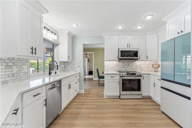 kitchen with appliances with stainless steel finishes, sink, white cabinets, light stone countertops, and light hardwood / wood-style floors