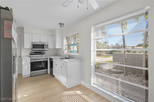 kitchen with white cabinets, light wood-type flooring, stainless steel appliances, sink, and ceiling fan