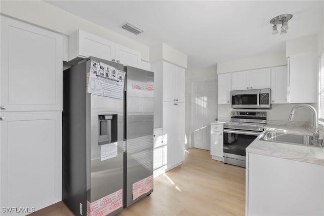 kitchen with appliances with stainless steel finishes, sink, white cabinets, and light hardwood / wood-style floors