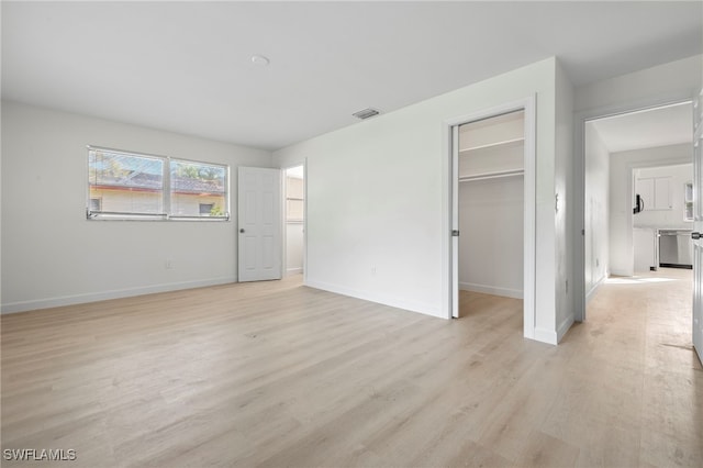 unfurnished bedroom featuring a walk in closet, a closet, and light wood-type flooring