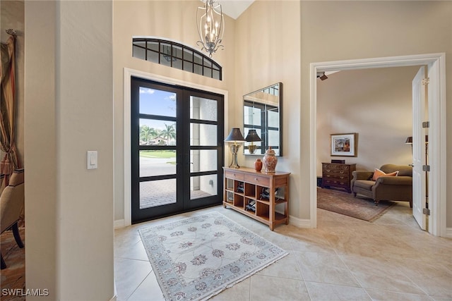 tiled foyer entrance with a high ceiling, french doors, and a notable chandelier